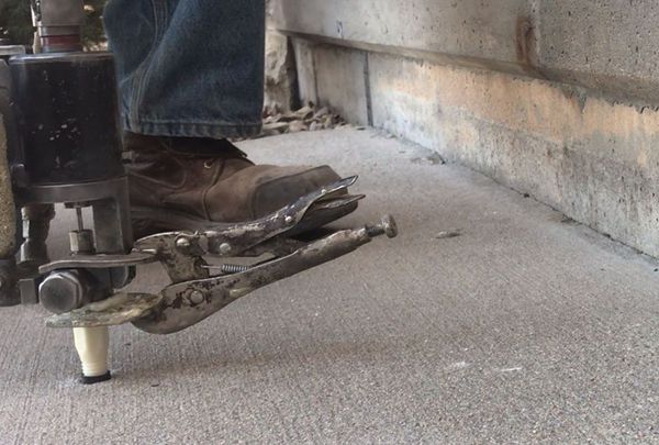 Person using pliers to work on concrete near a building's base. Visible: work boot, tool.