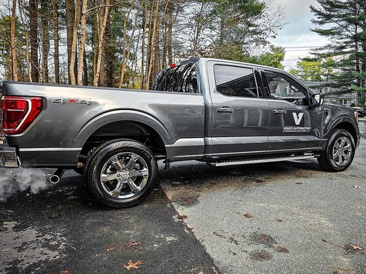 A gray pickup truck is parked in a driveway next to trees.