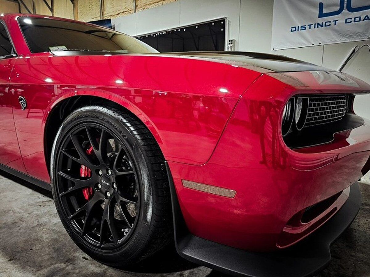 A red dodge challenger is parked in a garage next to a flag.