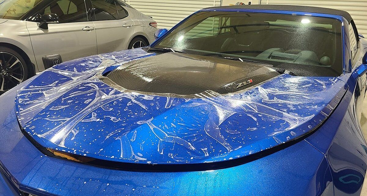 A blue car is covered in plastic wrap.