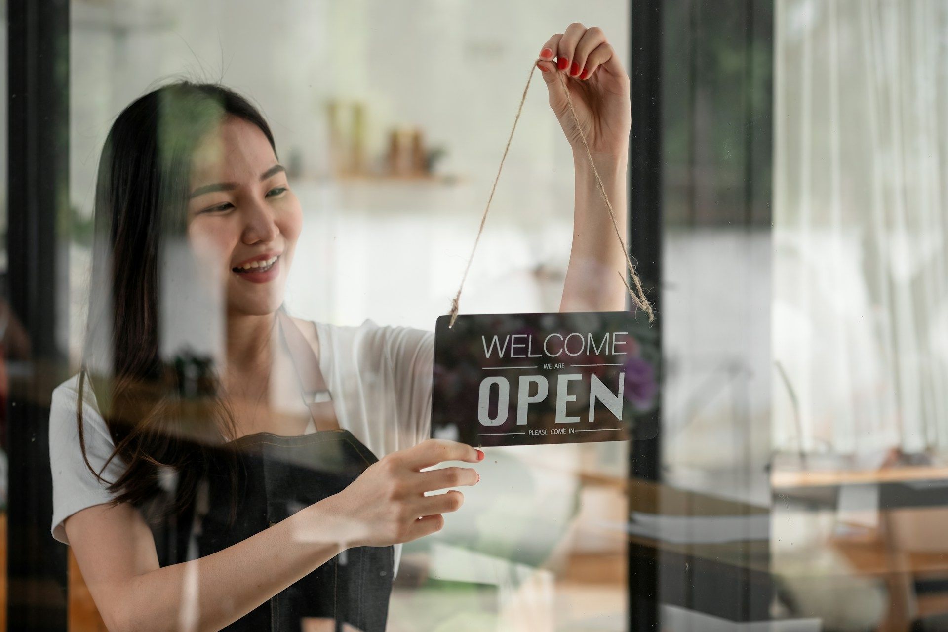 Smiling woman turning 'Welcome OPEN' sign on glass door
