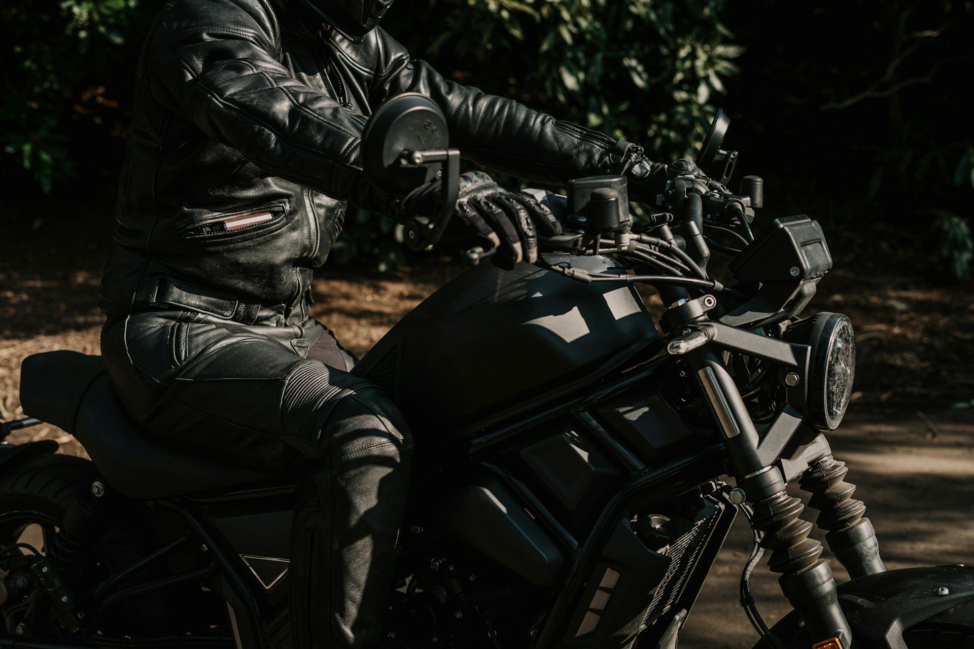 Close up profile of a motorcycle rider wearing a black leather jacket sitting on a bike