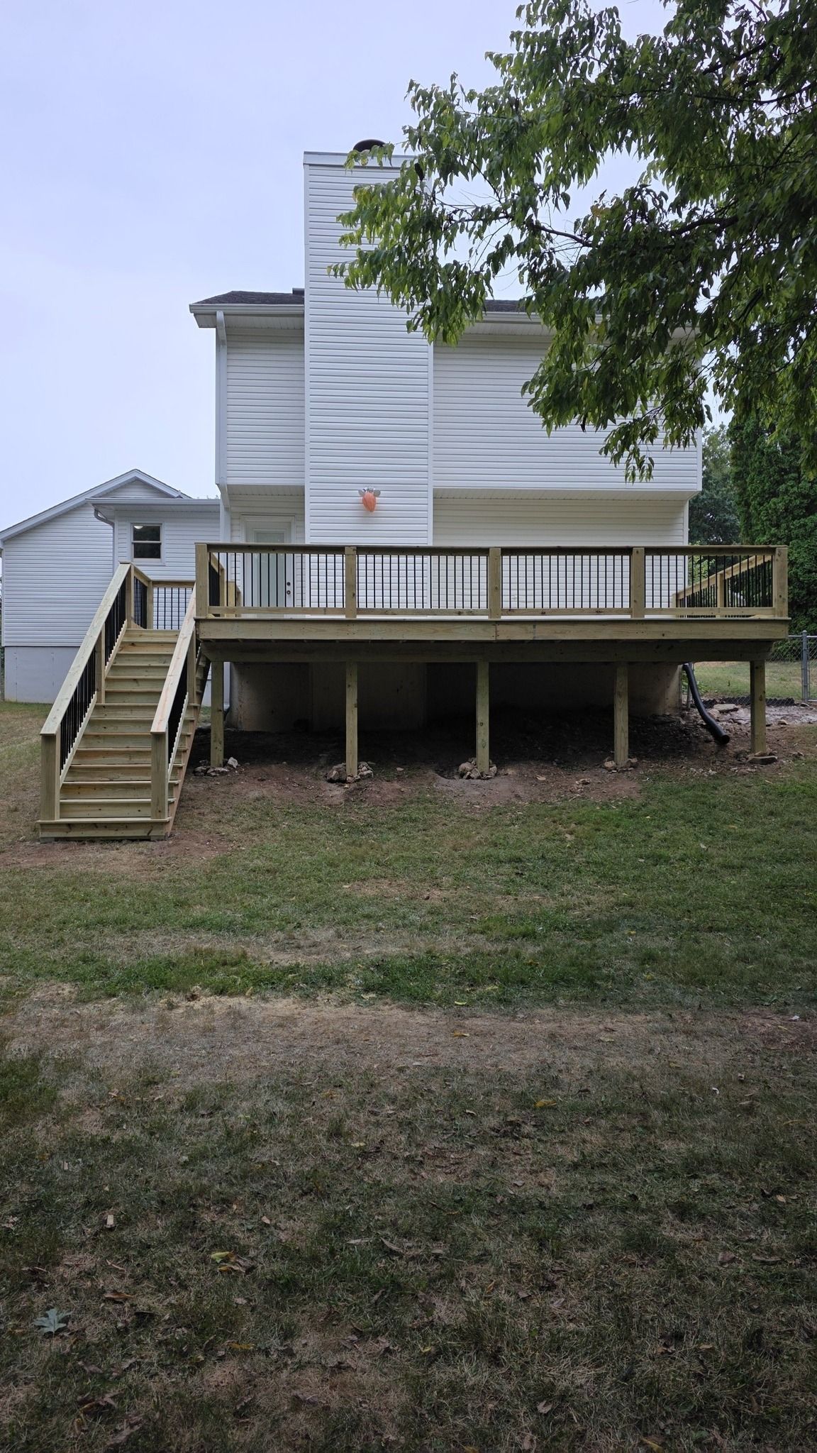 A white house exterior featuring a newly built wooden deck with a staircase leading down to a grassy backyard.