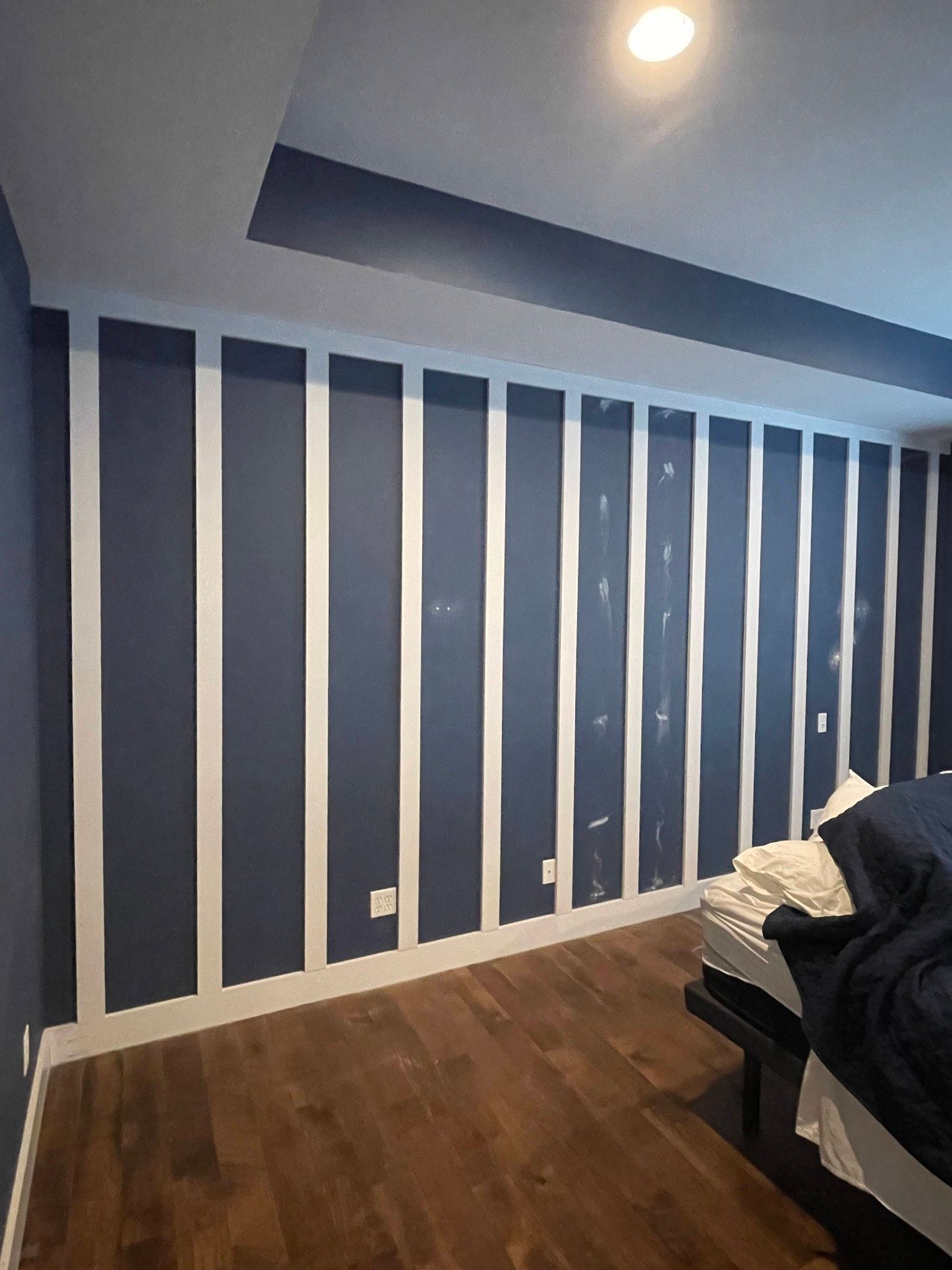 A blue bedroom wall features vertical white wood slats or battens, creating a striped accent wall above a wooden floor.