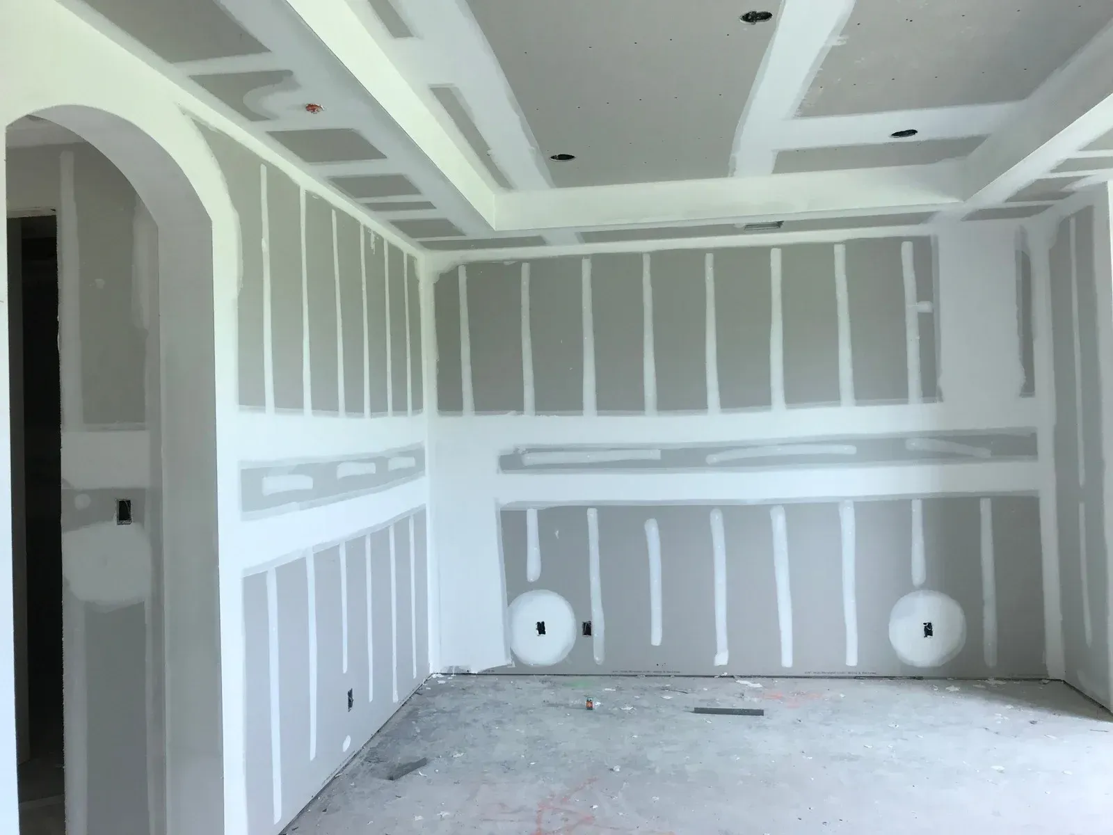 Unfinished drywall room with white joint compound lines, arched doorway, and construction debris on the floor