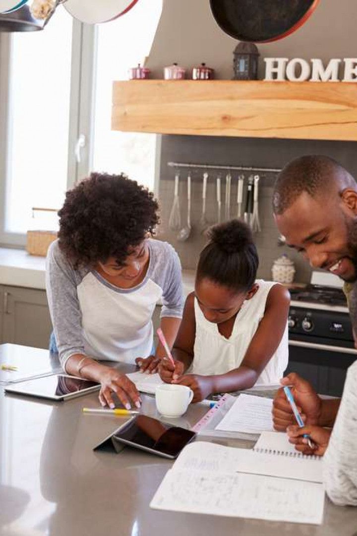 People gathered around a kitchen counter reviewing papers and a tablet in a bright home kitchen.