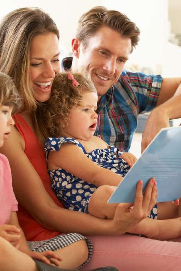 Family sitting on a couch, smiling and reading a book together.