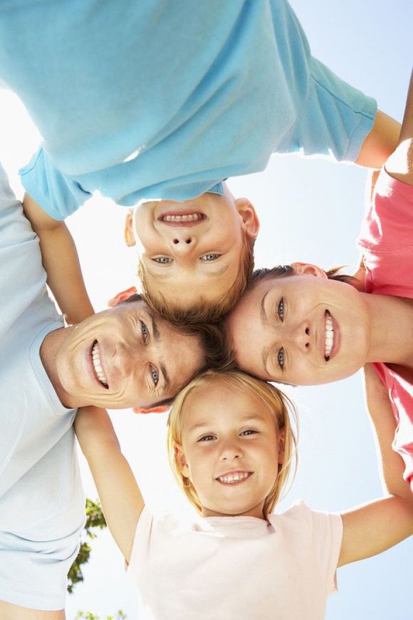 Smiling children lying in a circle and looking up at the camera outdoors