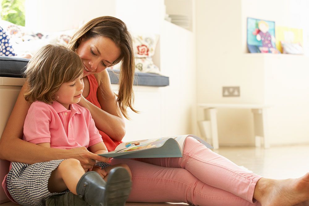Woman reading a book with a child on a couch in a bright living room