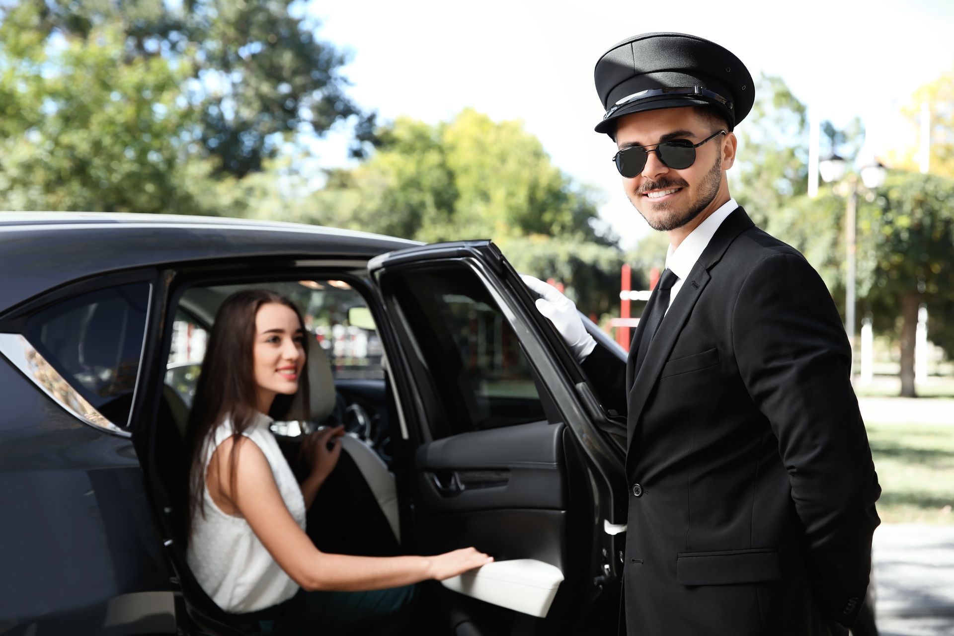 Driver smiling at a black car while a passenger sits in the back seat outside.