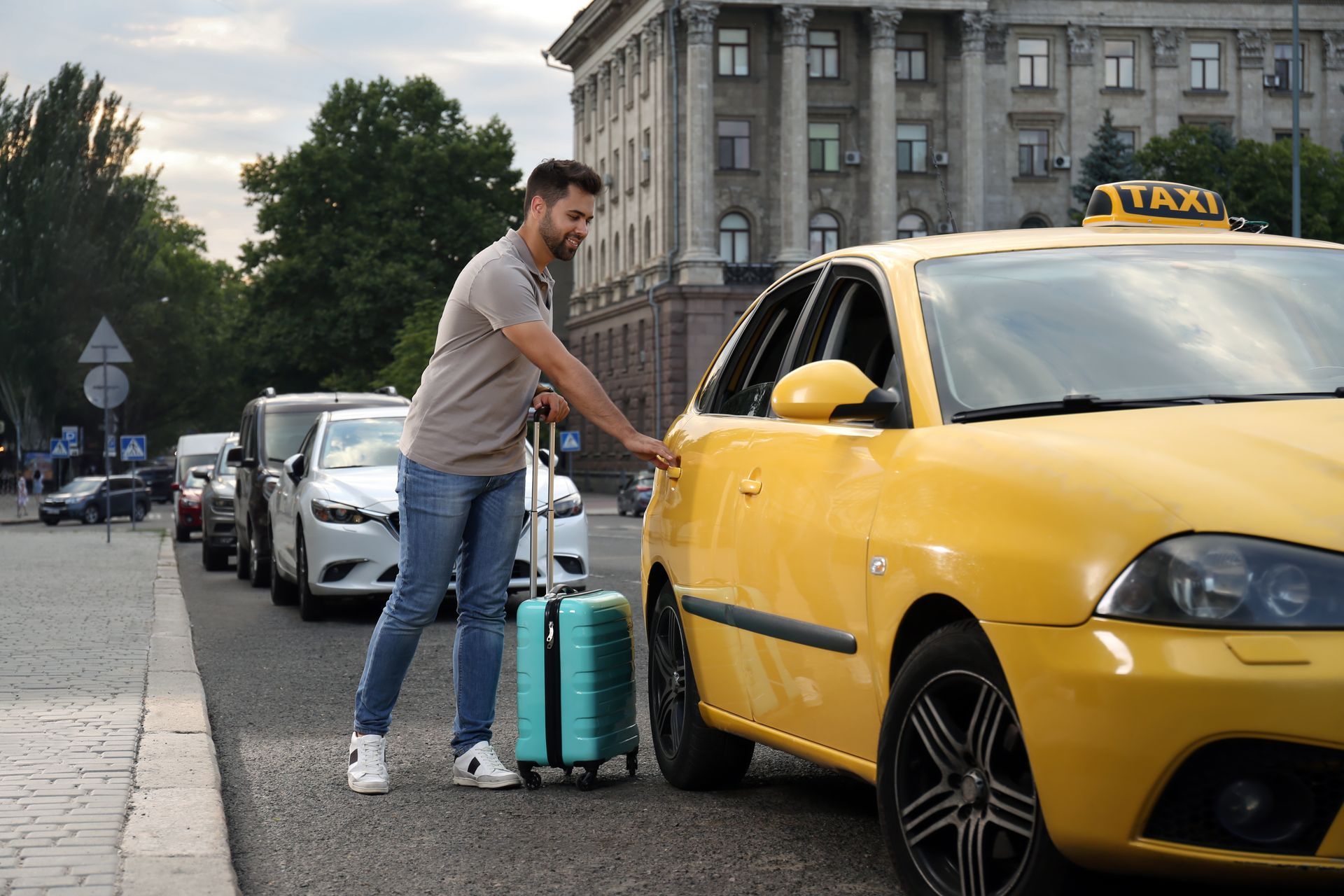 Man with rolling suitcase beside yellow taxi on a city street