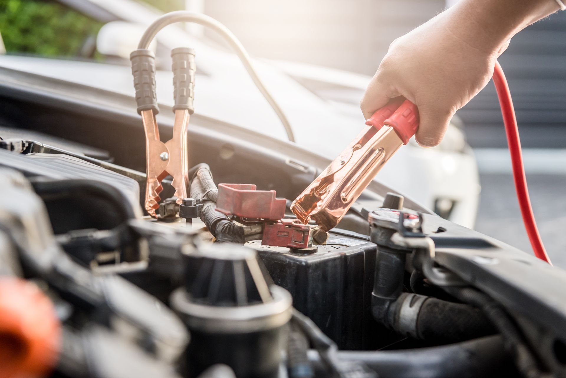 Hand using jumper cables to connect a car battery in an open engine bay