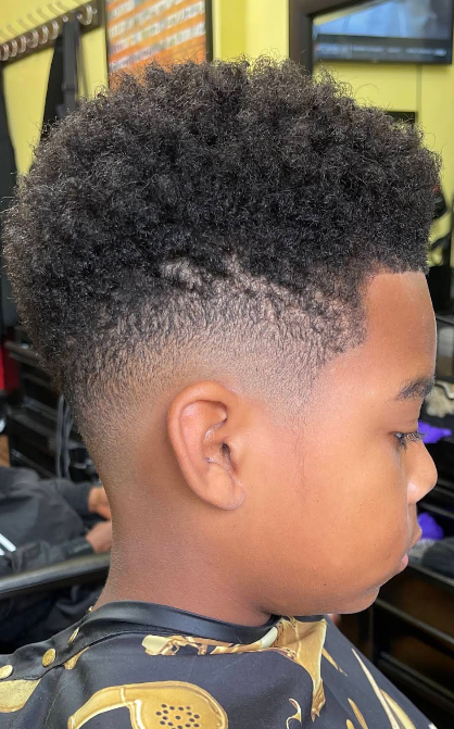 Side profile of a child with a short curly fade haircut in a barbershop chair