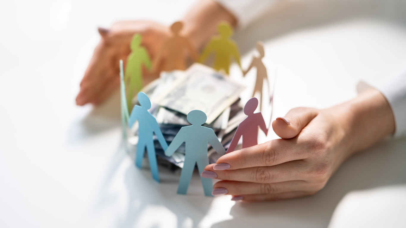 Hands protecting money within a circle of paper people, symbolizing community and financial security.