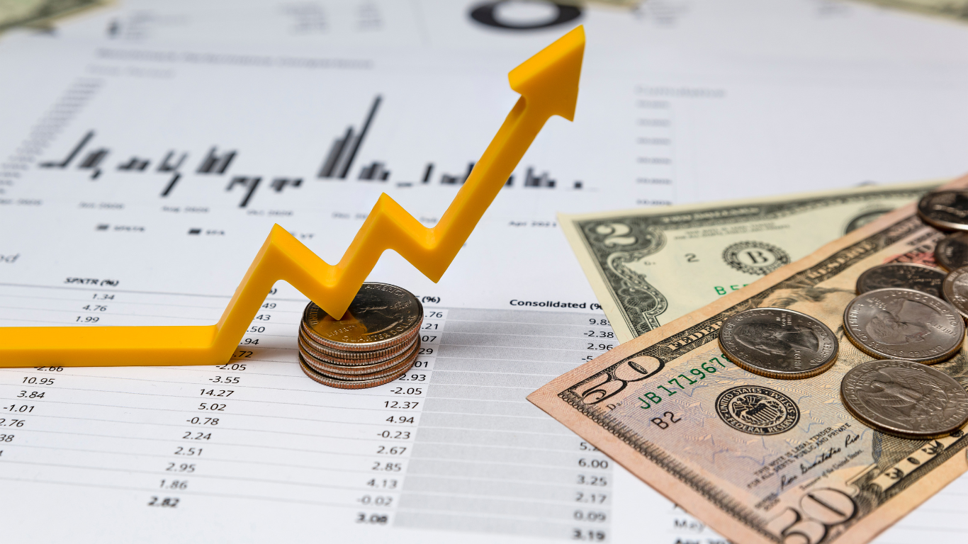 A yellow arrow pointing up rests on coins, with money and a graph in the background, indicating financial growth.