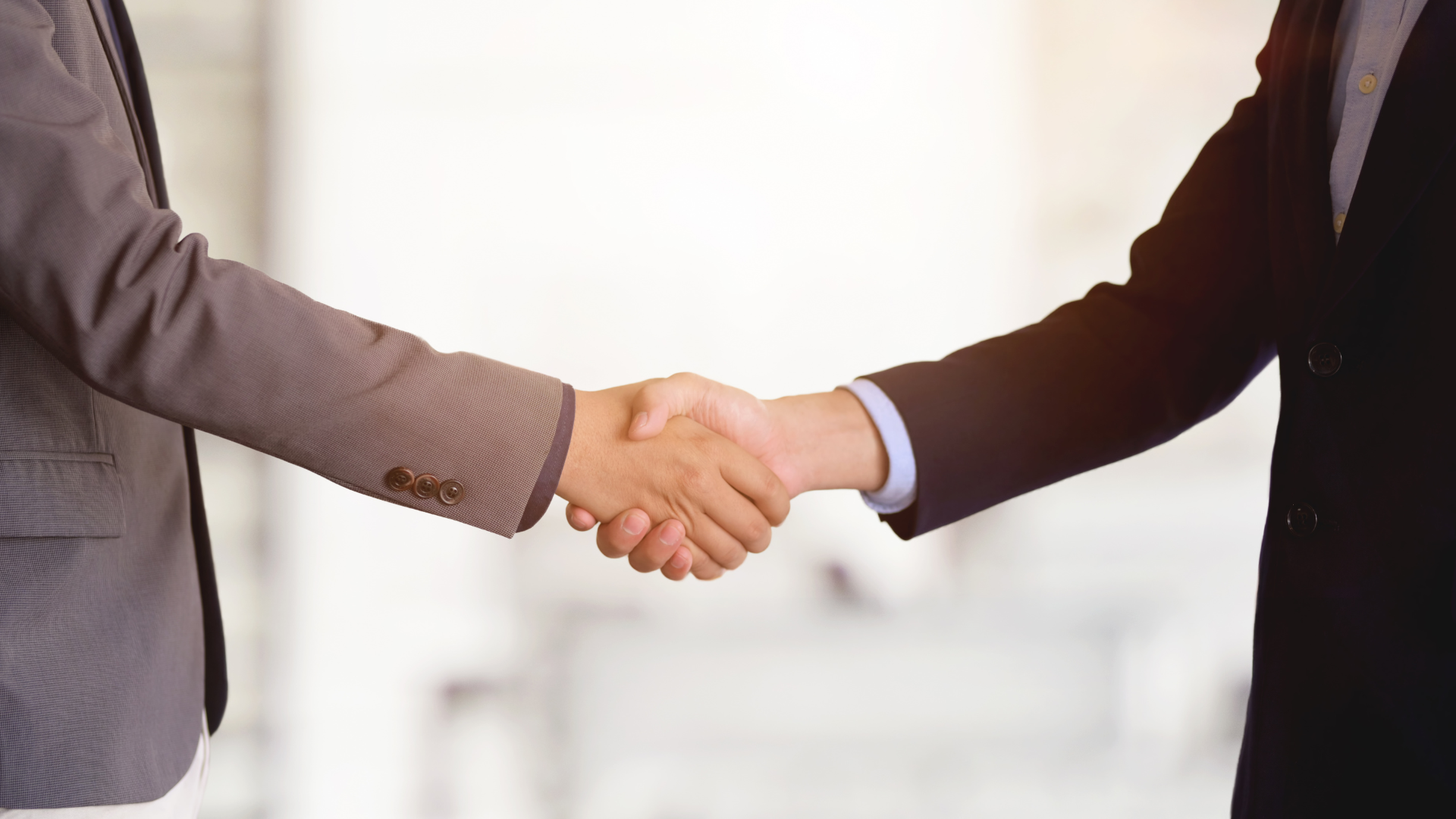 Two people in suits shaking hands, indoors.