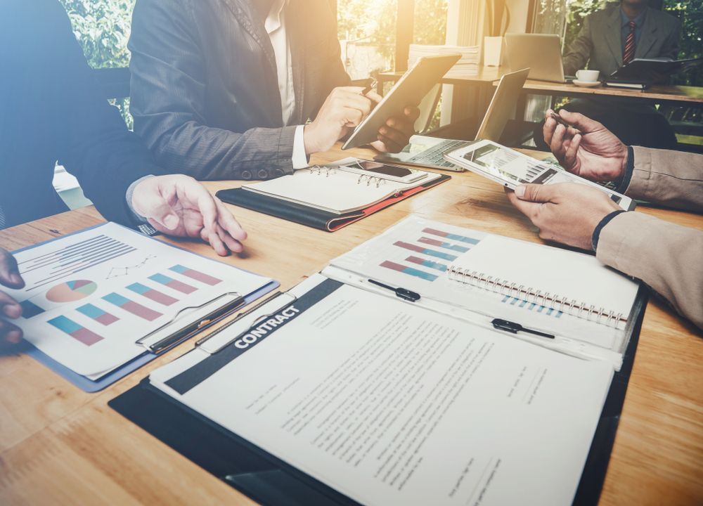 Business Professionals Reviewing Documents and Financial Charts Around a Wooden Table, Likely in a Meeting — C & D Manufacturing In Caboolture, QLD