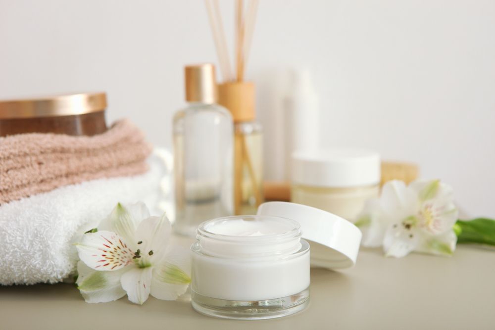 A Jar of White Cream With an Open Lid Sits in Front of Other Spa-themed Products and White Flowers — C & D Manufacturing In Caboolture, QLD