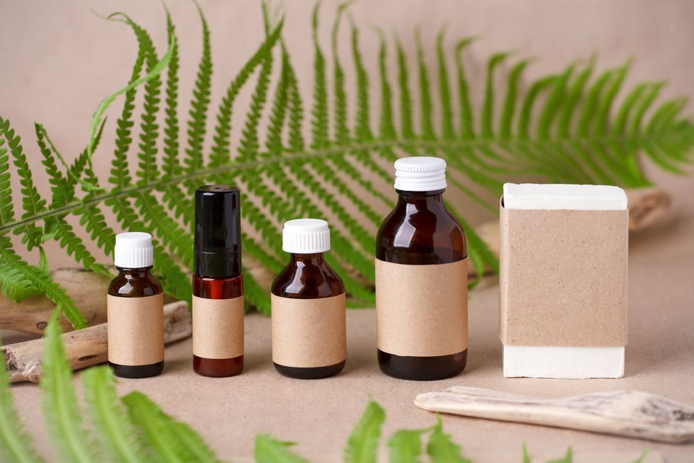 Bottles of Various Sizes With Brown Labels, in Front of Green Fern Leaves and Wooden Twigs — C & D Manufacturing In Caboolture, QLD