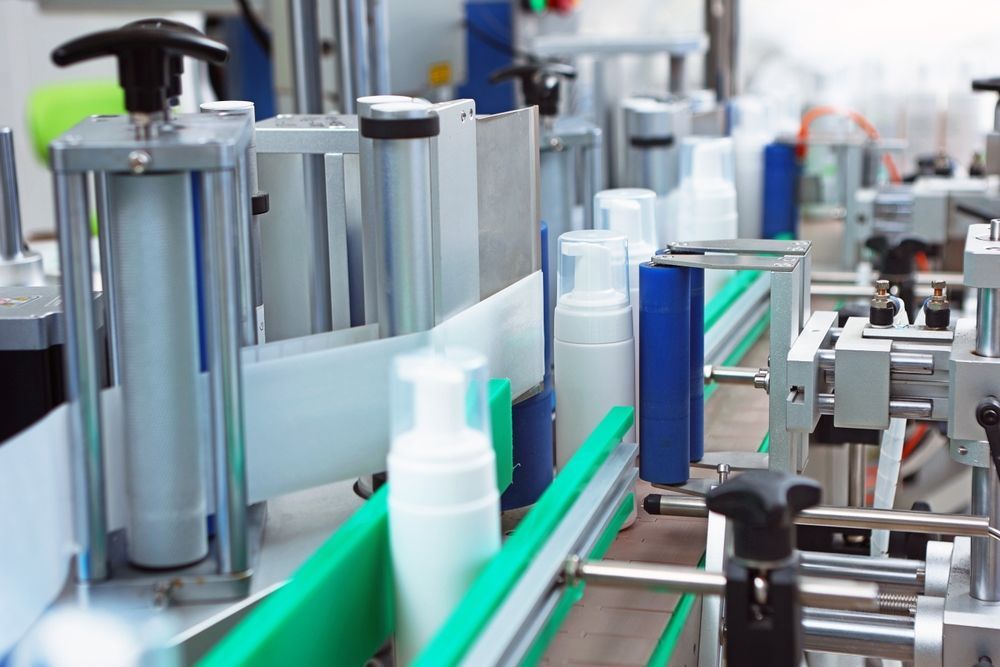Bottles on a Conveyor Belt Being Labeled in a Factory. the Machines Are Gray and White, and the Belt is Green — C & D Manufacturing In Caboolture, QLD