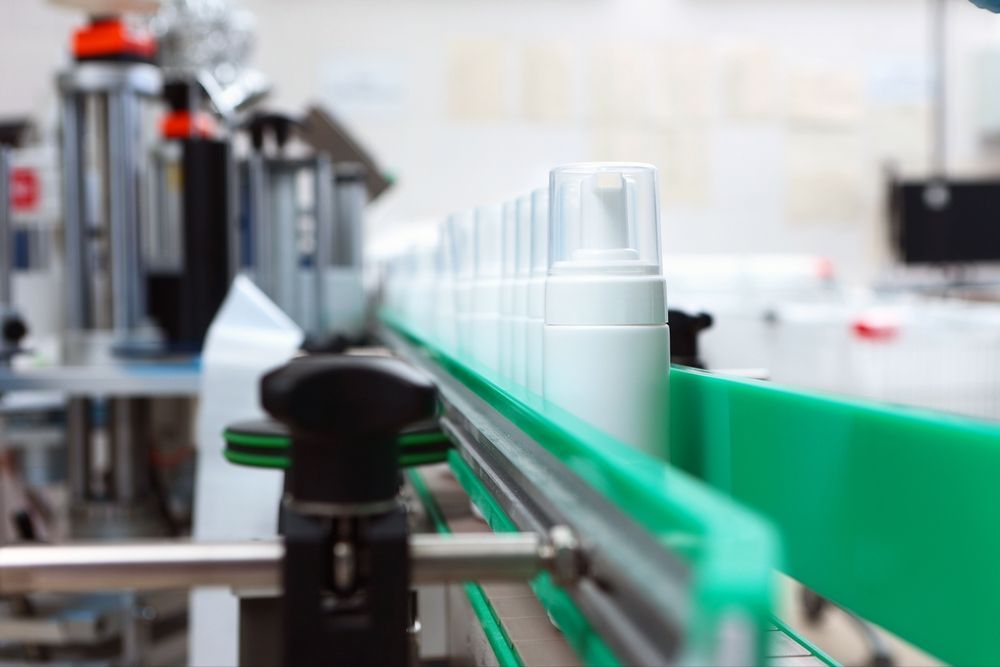 White Cosmetic Bottles With Pump Tops Moving Along a Green Conveyor Belt in a Factory — C & D Manufacturing In Caboolture, QLD