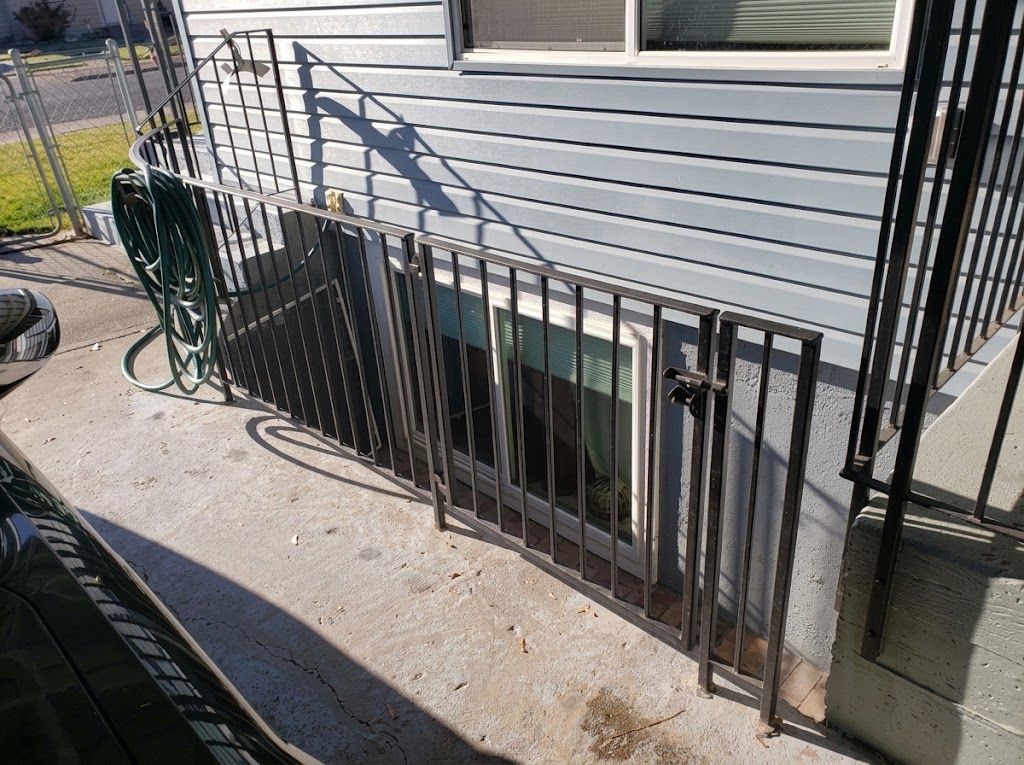 Black metal railing along a basement window beside a white-sided house and concrete walkway