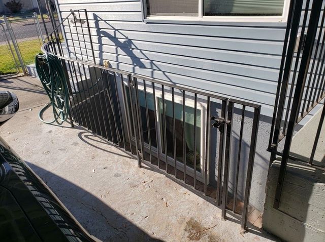 Black metal railing along a basement window beside a white-sided house and concrete walkway