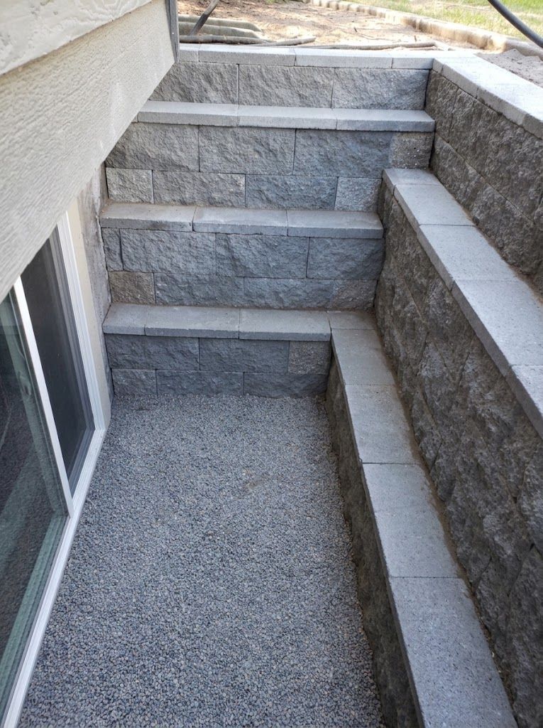 Narrow concrete stairwell descending to a basement window well with stone retaining walls