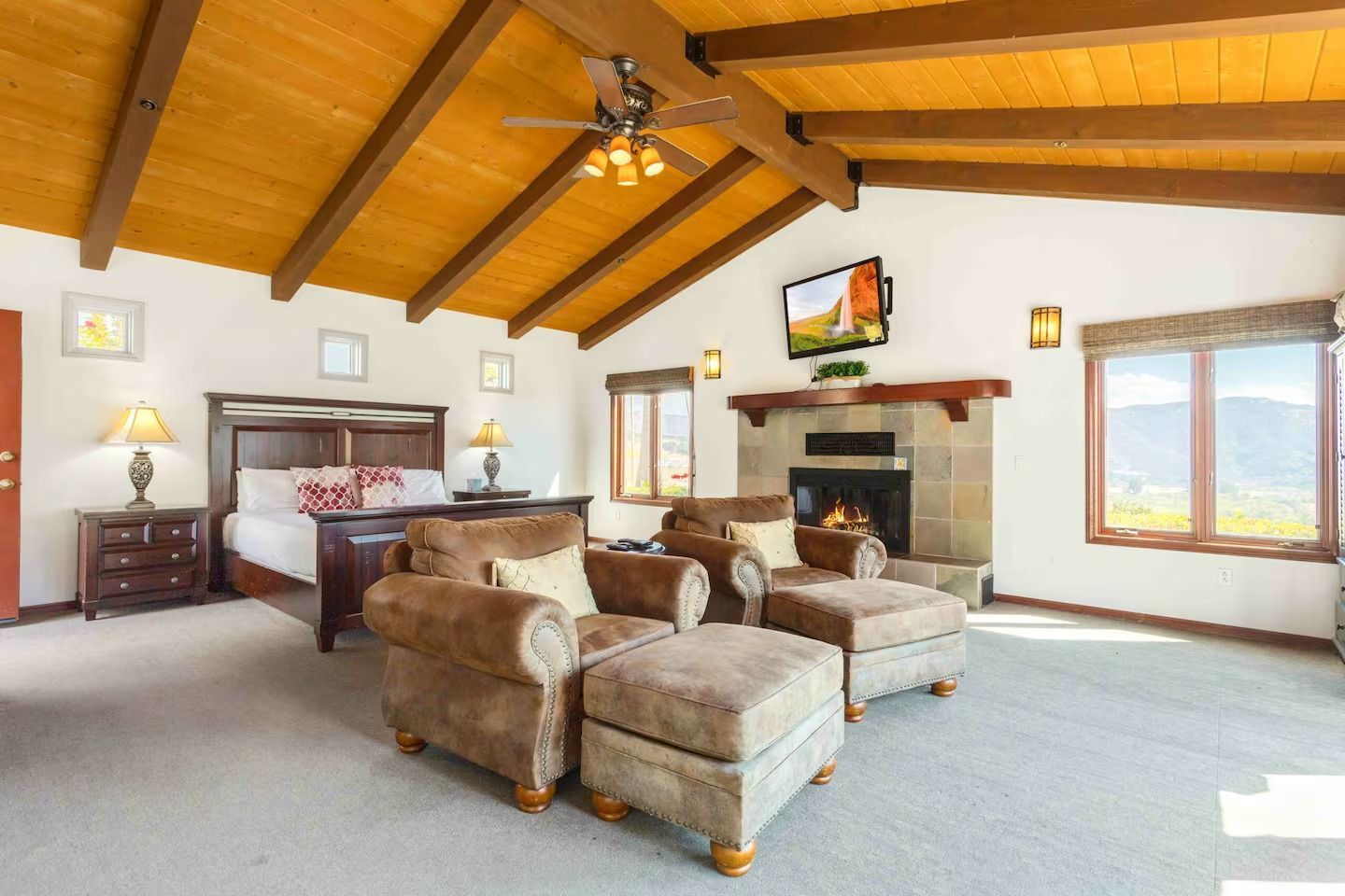 Spacious bedroom with a bed, fireplace, seating area, and wooden ceiling.