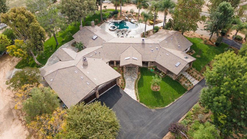 Aerial view of a large, multi-winged house with a pool, set amid greenery and trees.