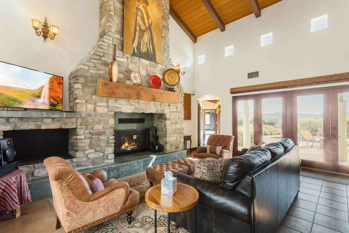 Living room with stone fireplace, brown leather couch, and large windows.