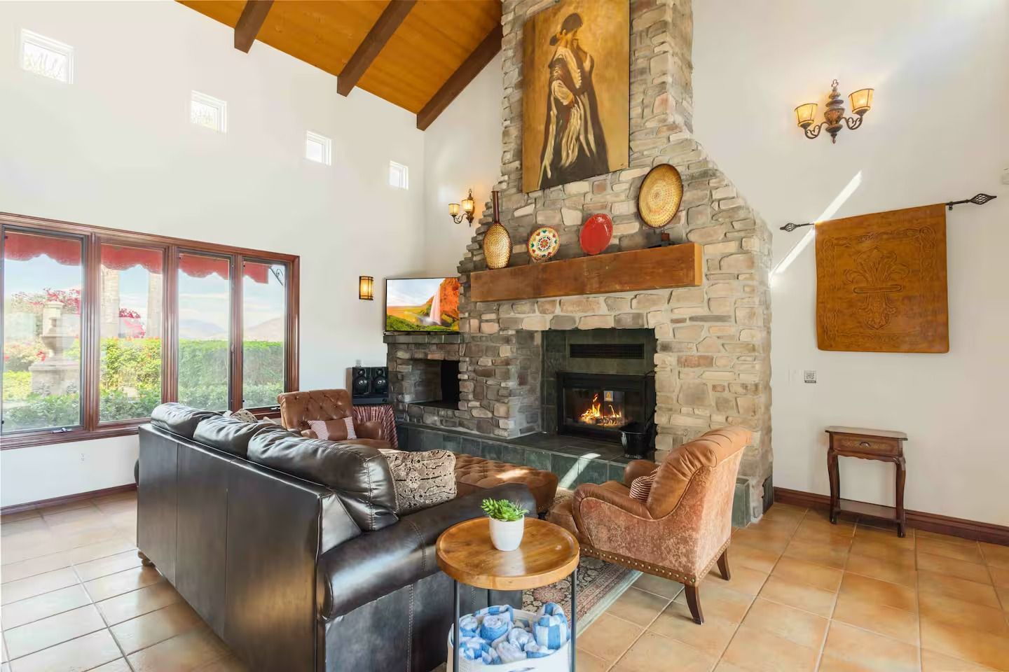 Living room with stone fireplace, brown leather sofa, and large windows.