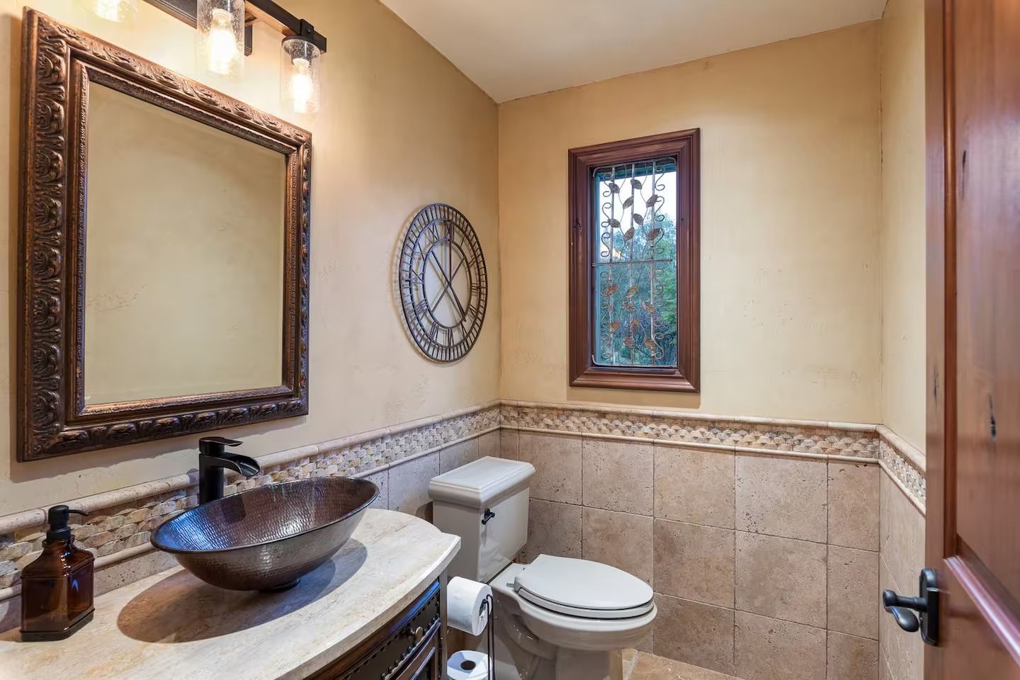 Bathroom with a stone tile backsplash, patterned mirror, vessel sink, and a clock.