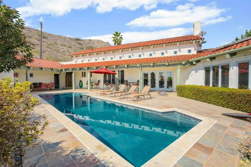 Swimming pool in courtyard of white stucco house with red tile roof; mountains in the background.
