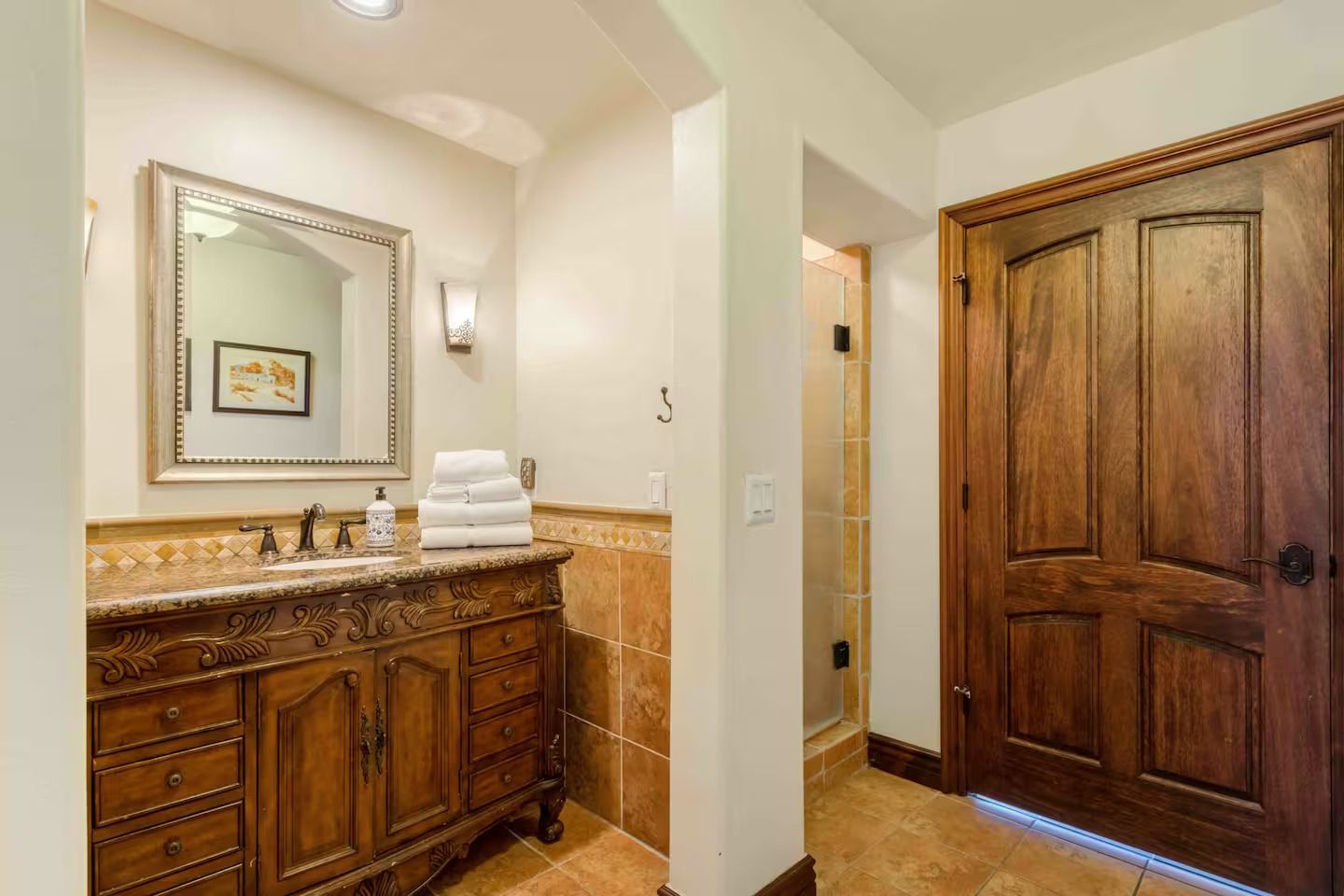 Bathroom with wooden vanity, tile, and a framed mirror. A shower and wood door are also visible.