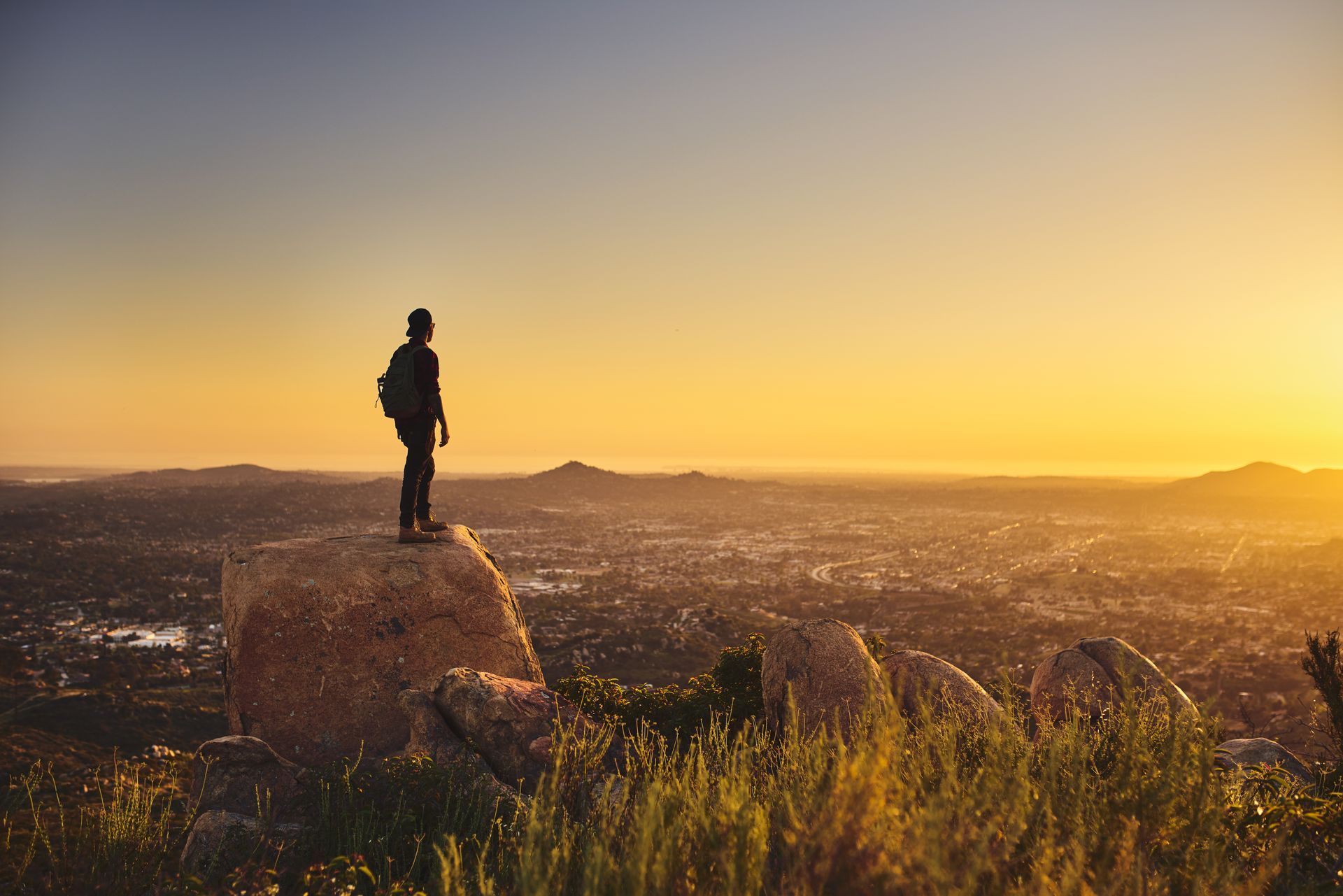 Silhouette of a person standing on a rocky hill at sunset overlooking a cityscape