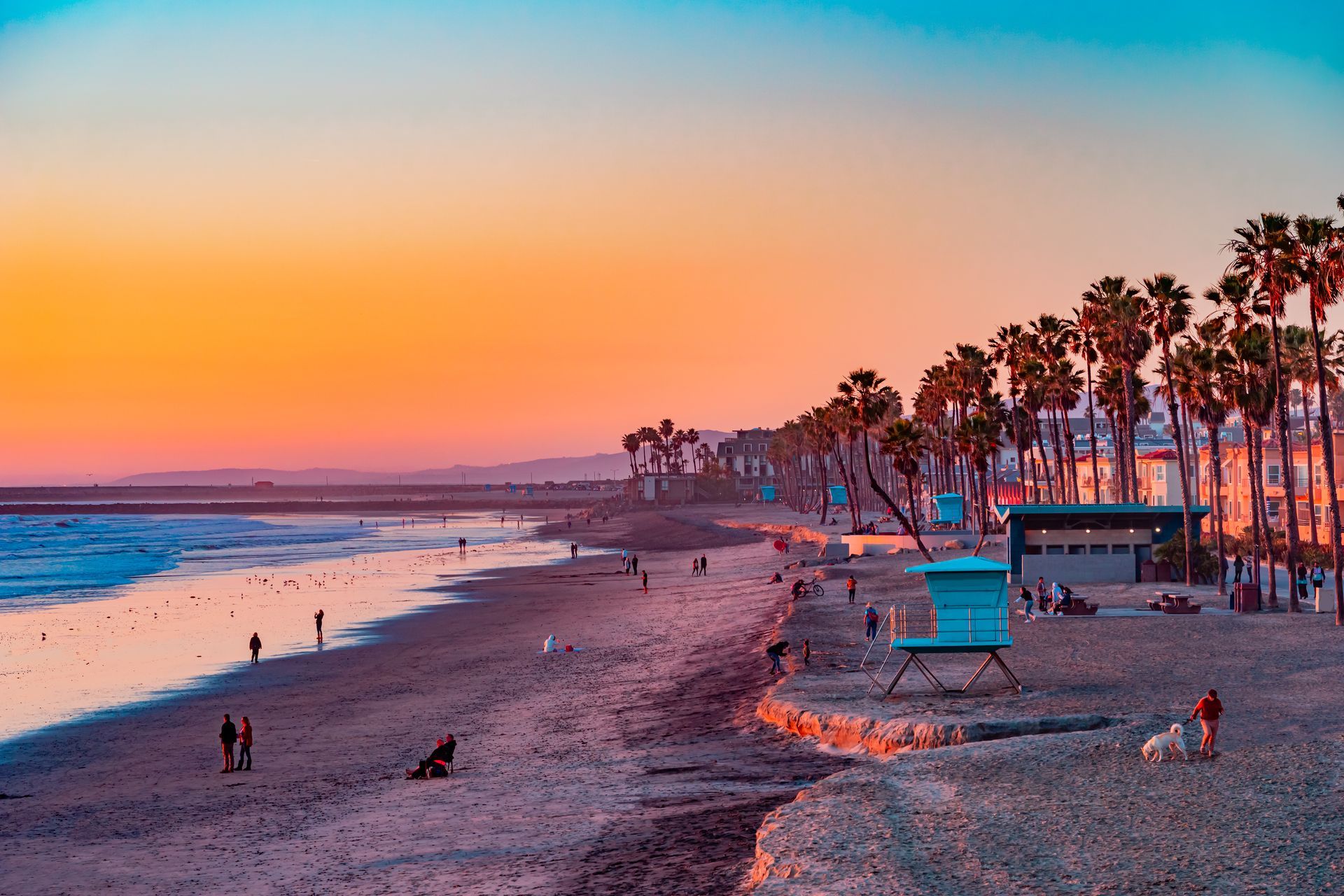 Sunset beach with waves, palm trees, and a lifeguard tower along the shore