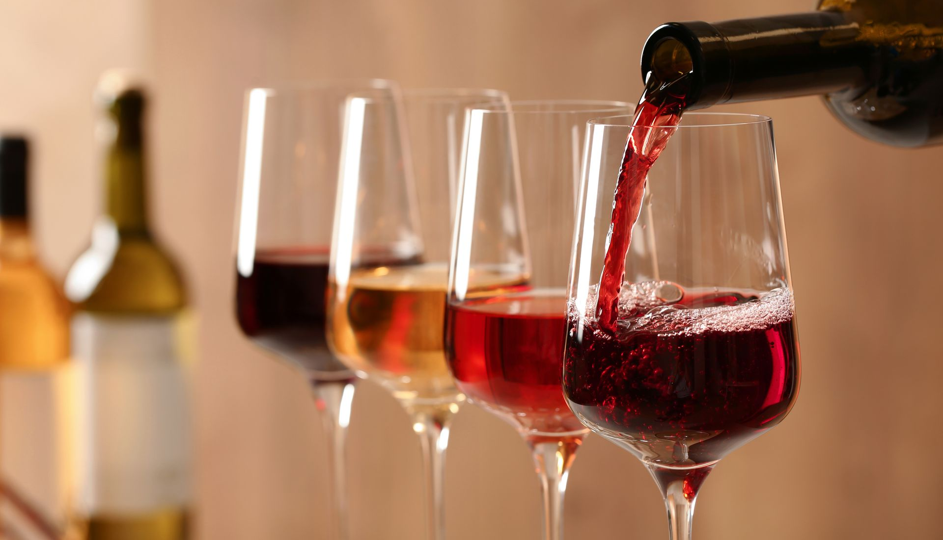 Red wine is being poured into a glass, with three other glasses filled with various wines in the background.