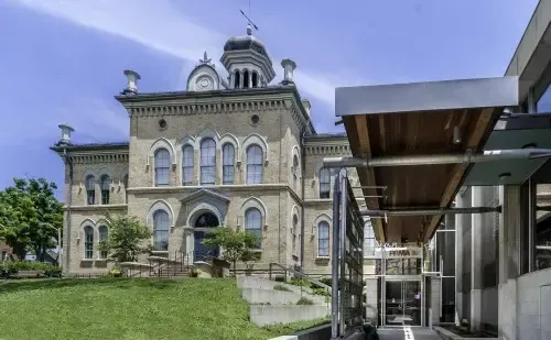 Historic stone building beside a modern glass walkway under a blue sky