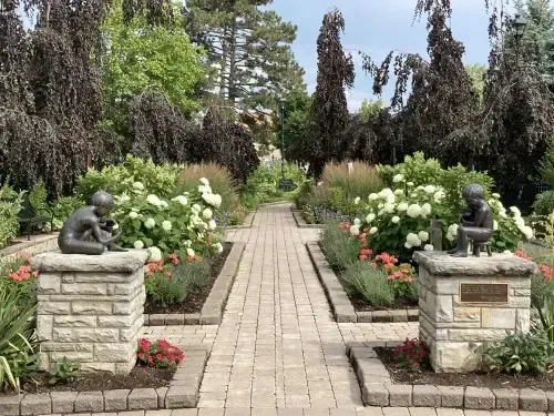 Formal garden path with stone statues, white flowers, and tall trees