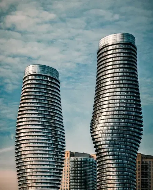 Two curved glass skyscrapers against a cloudy sky, one taller than the other