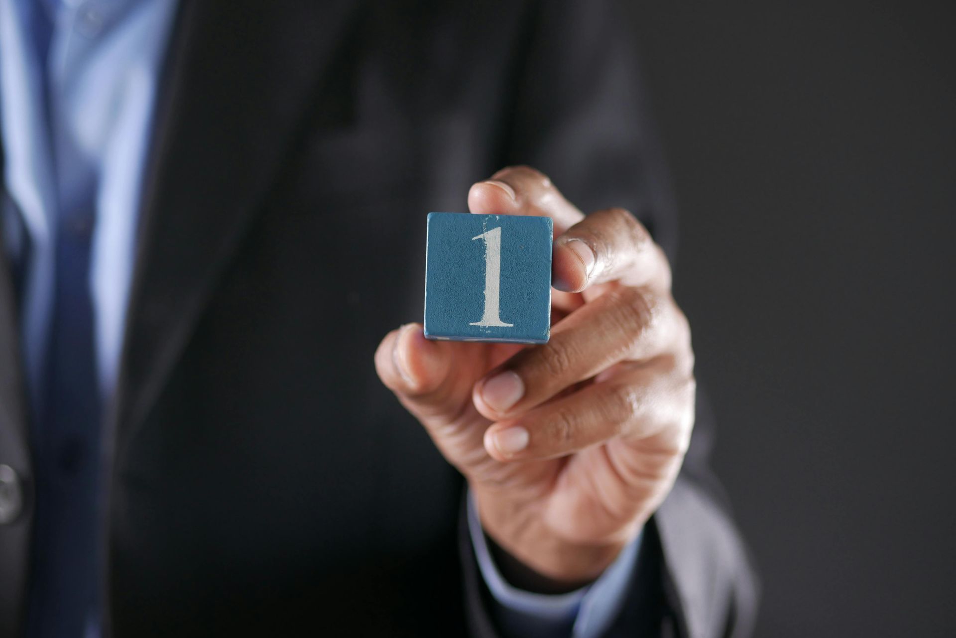 Hand in suit holding a blue block with the number 1 | Financial Consultant Top 10 in Mississauga