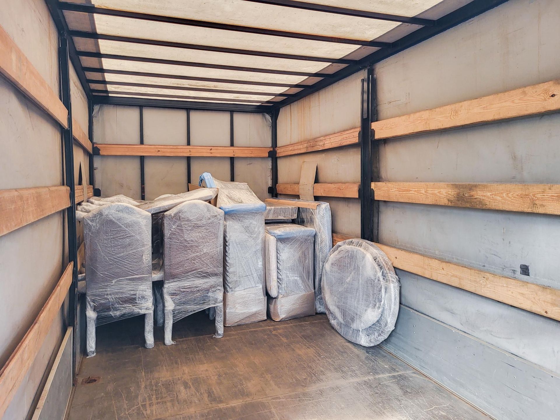 Furniture wrapped in plastic inside a truck bed, ready for transport.