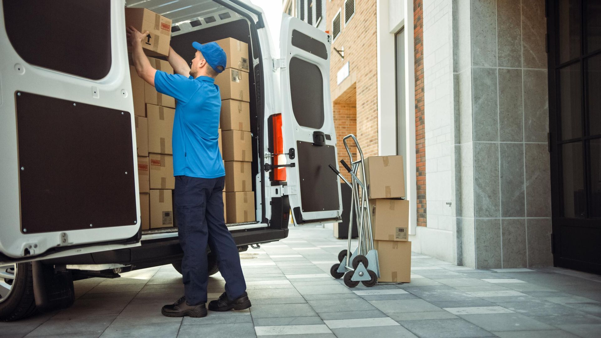 Delivery person loading packages into van near building.