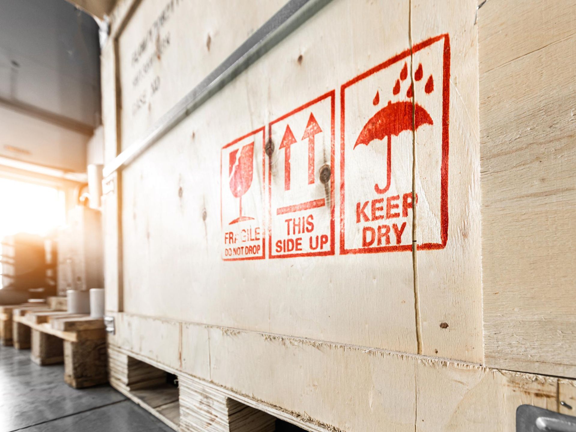 Wooden crate with red shipping symbols: fragile, side up, and keep dry.