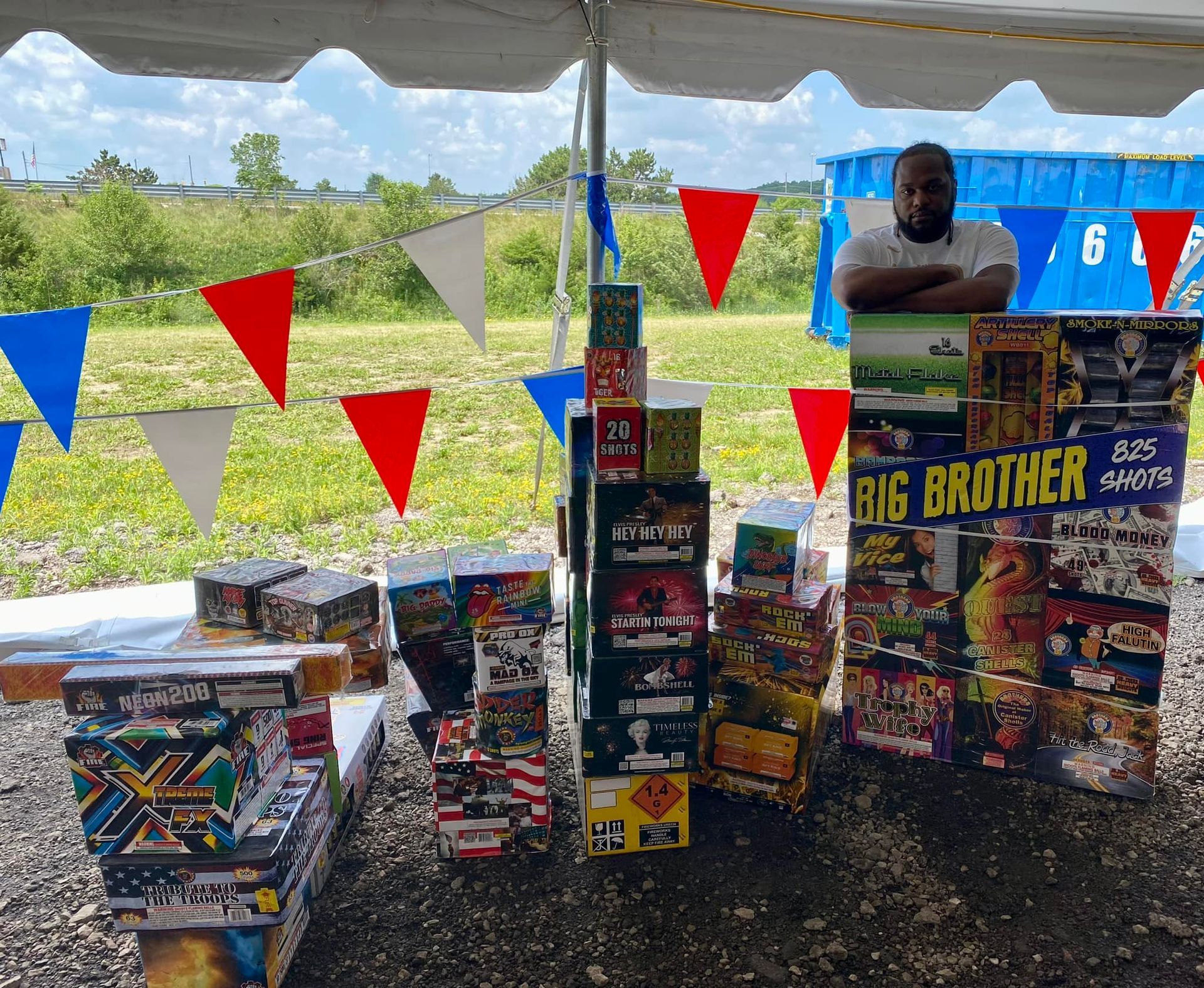A man is standing in front of a display of fireworks under a tent.