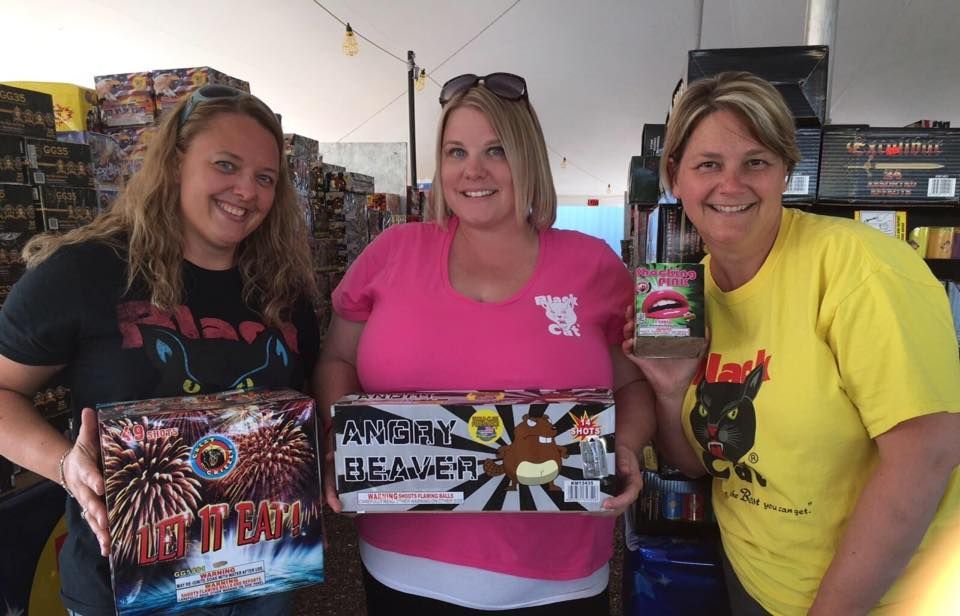 Three women are standing next to each other holding boxes of fireworks.