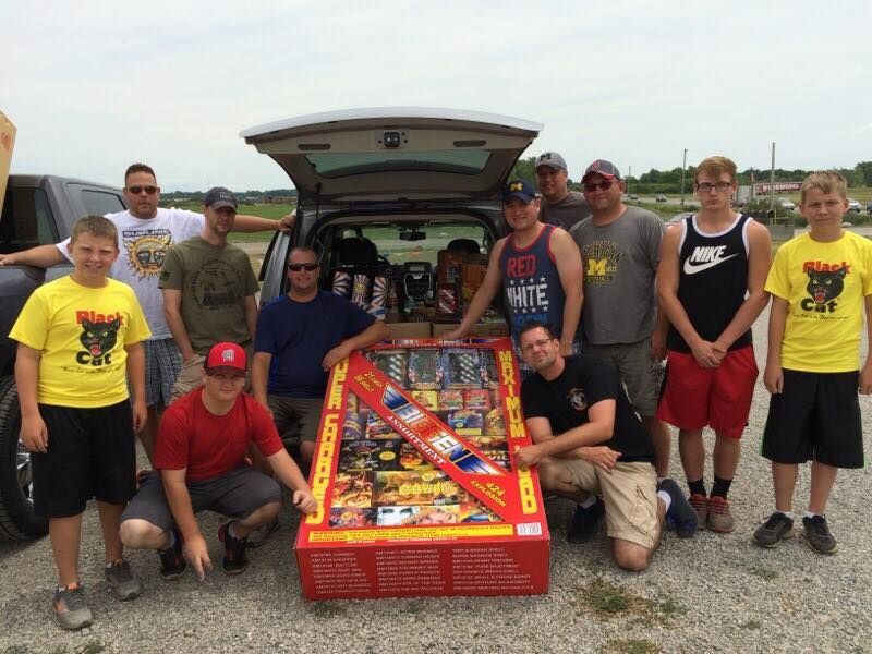 A group of men are posing for a picture in front of a box of fireworks.
