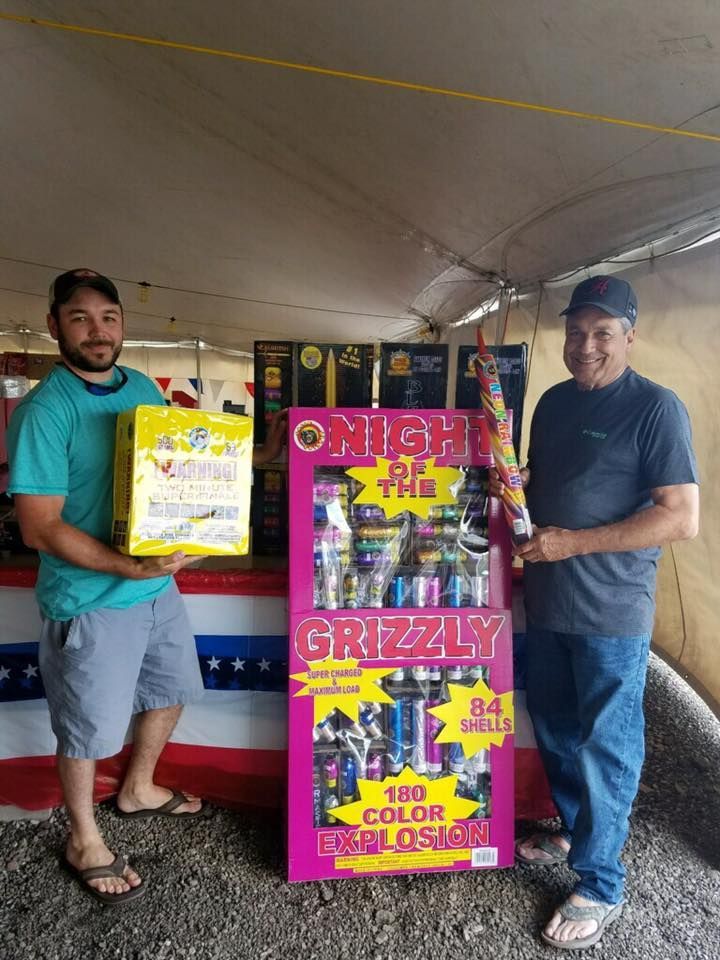 Two men are standing next to a display of grizzly fireworks.