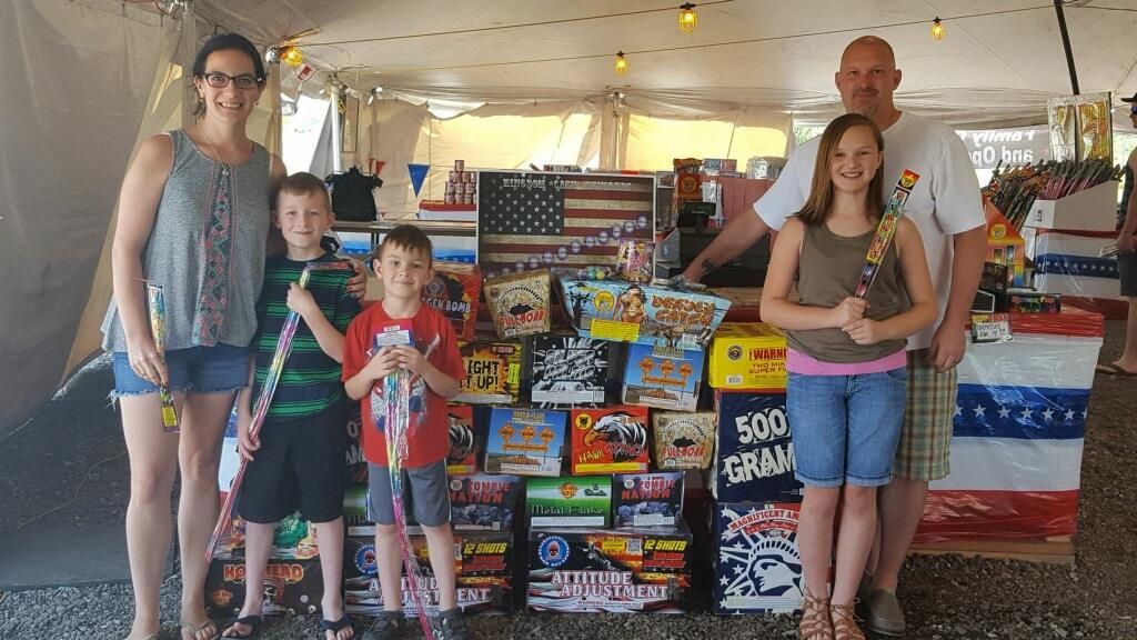 A family is standing in front of a table full of fireworks.